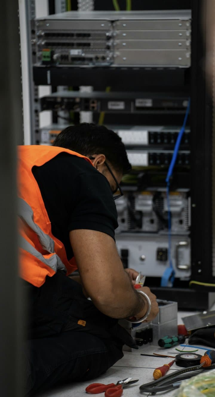 A technician at work on network equipment in a rack, tools on the floor.