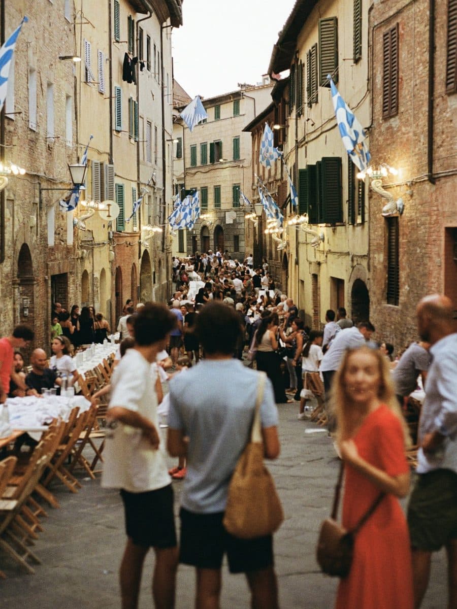Neighbors sharing a long dinner table in the street of an old town, under festive flags.