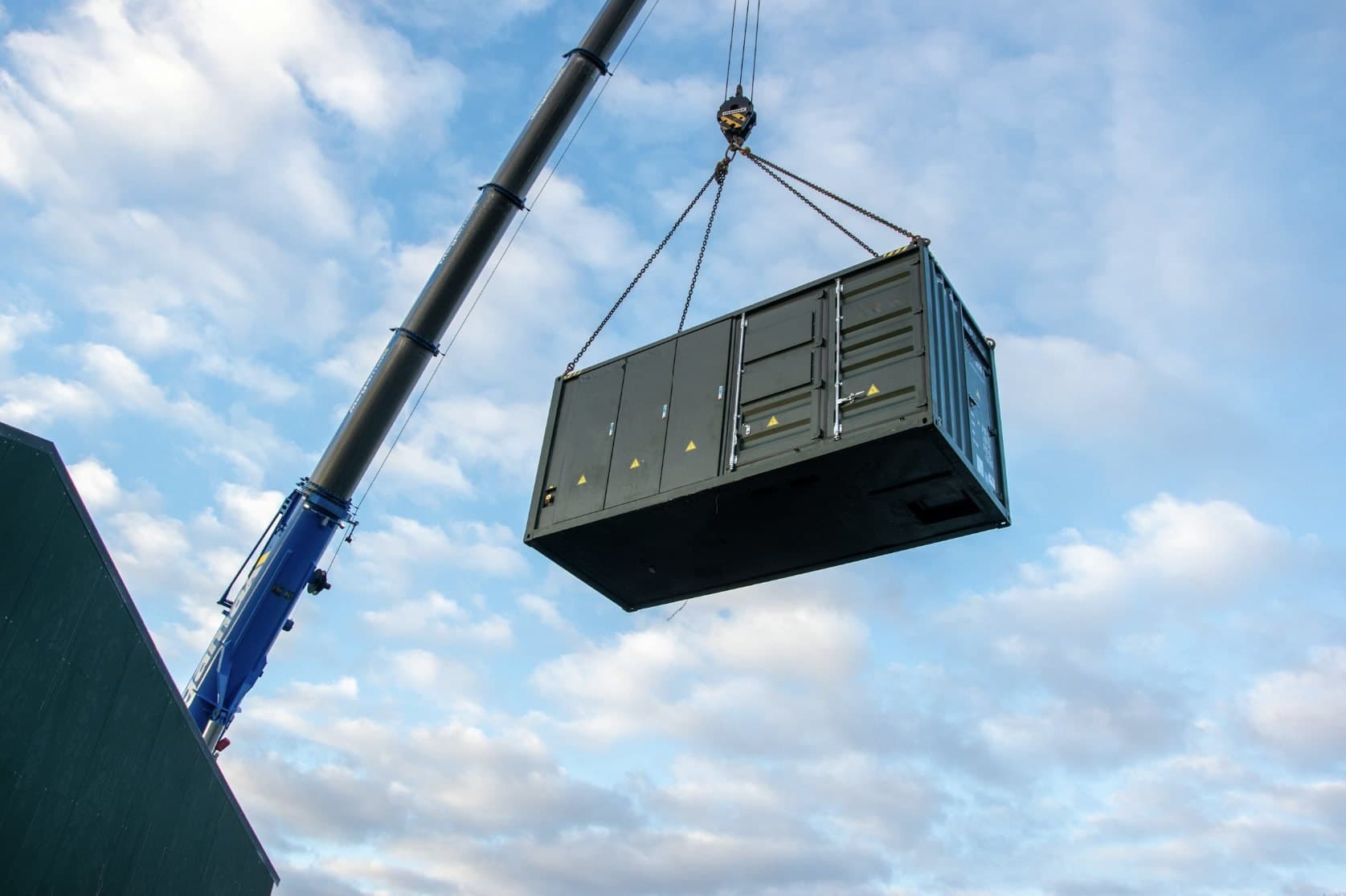 A crane lifting a prefabricated power module into place under a blue sky.