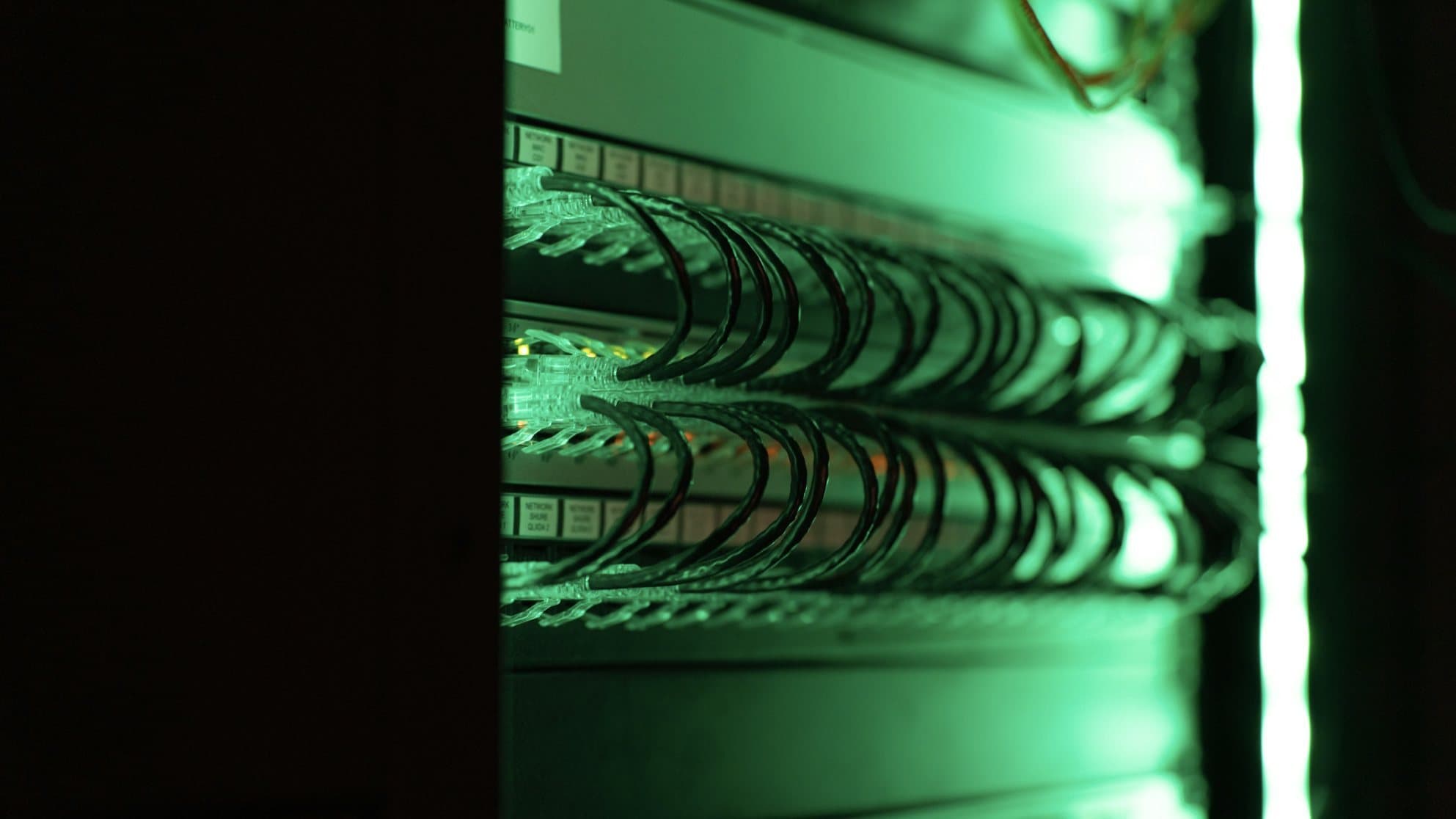 Network equipment in a rack, lit in green, with rows of cables.